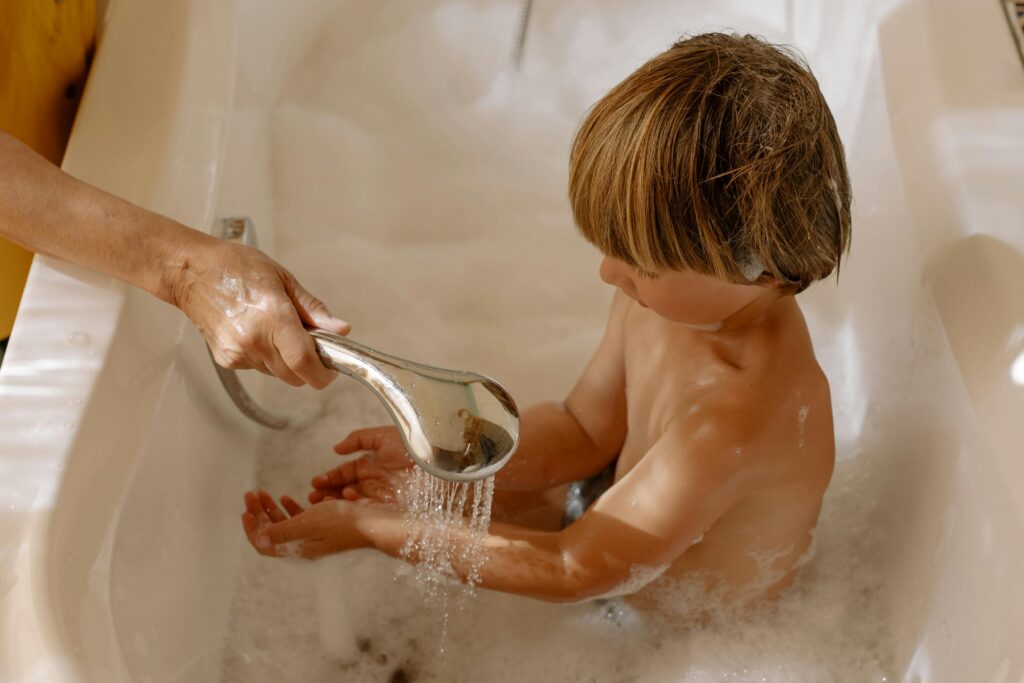 Young boy being washed by a parent in a bathtub, emphasizing hygiene and care.